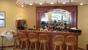 A bar area with a counter, multiple bottles, and wicker bar stools. - Tolon Holidays (Nafplio)