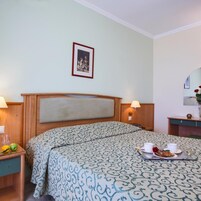 A hotel room with a bed, bedside tables, a lamp, a framed picture on the wall, and a tray with food and drinks.