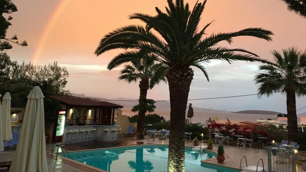 A pool area with a bar and lounge chairs, palm trees, and a view of the mountains. - Tolon Holidays (Nafplio)