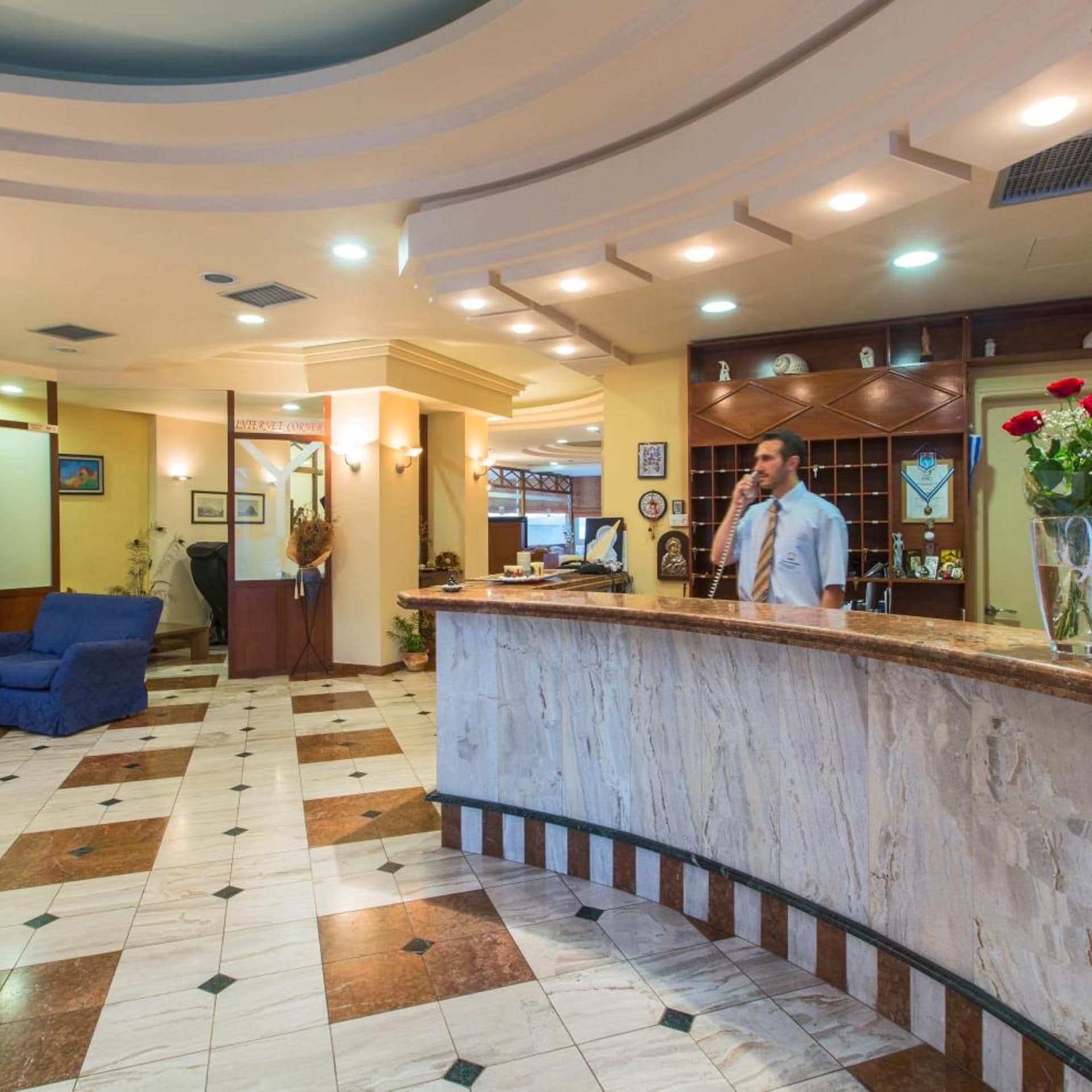 A hotel reception area with a marble counter, a blue sofa, and a decorative vase with flowers.