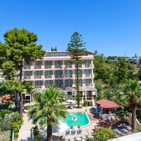 Un hotel de varios pisos con piscina, zona de estar exterior y abundante vegetación.