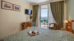 A hotel room with a bed, two chairs, a TV, a small table with a vase and flowers, and a balcony with a table and chairs. - Tolon Holidays (Nafplio)