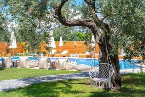 A poolside area with lounge chairs, a hanging chair, and a wooden fence. - Nefeli Hotel (Thasos)
