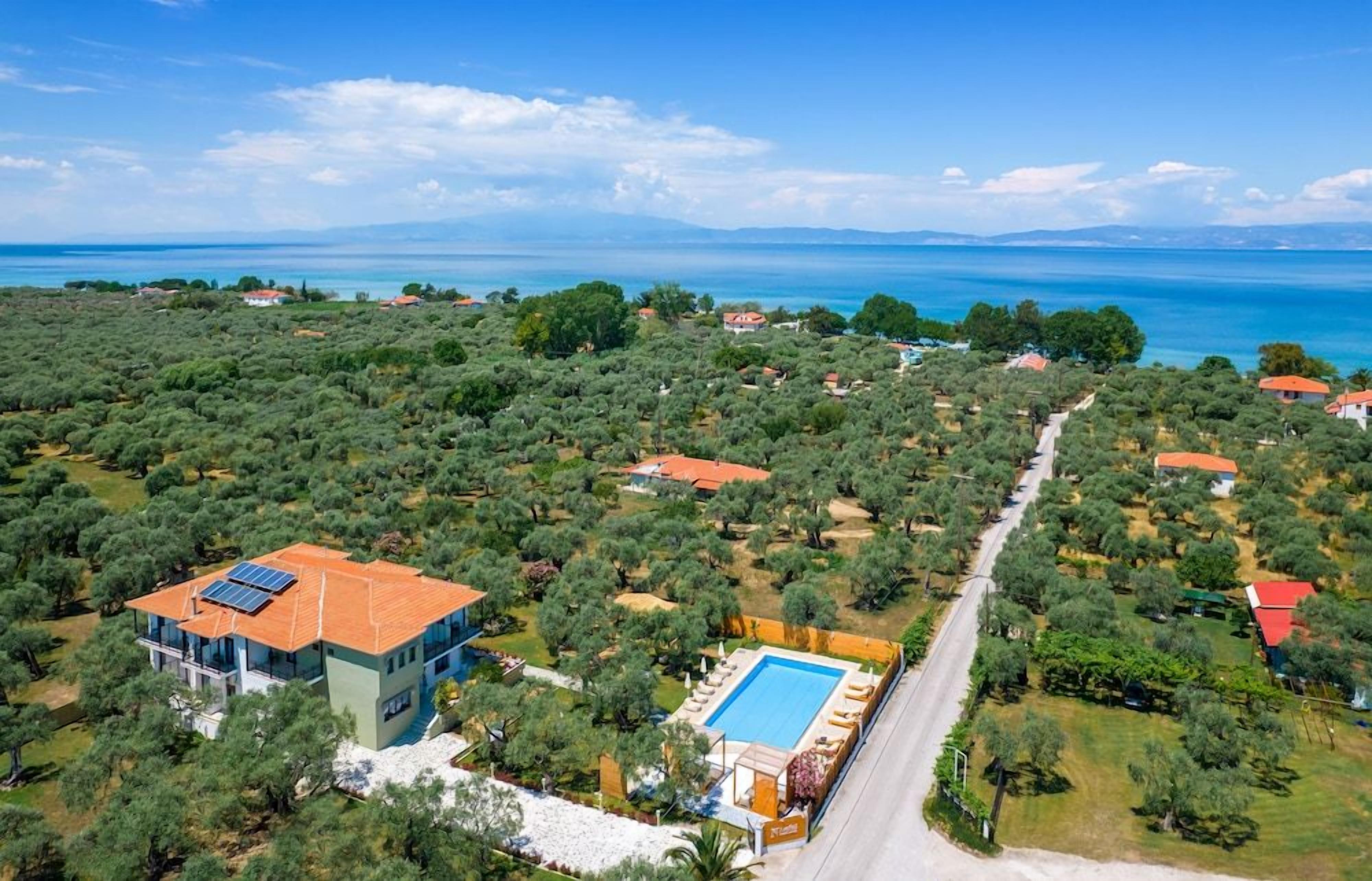 An aerial view of a coastal property with a swimming pool, solar panels, and a road leading to a cluster of houses.