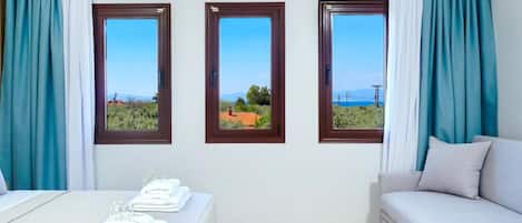 A hotel room with a bed, a sofa, and three windows with a view.