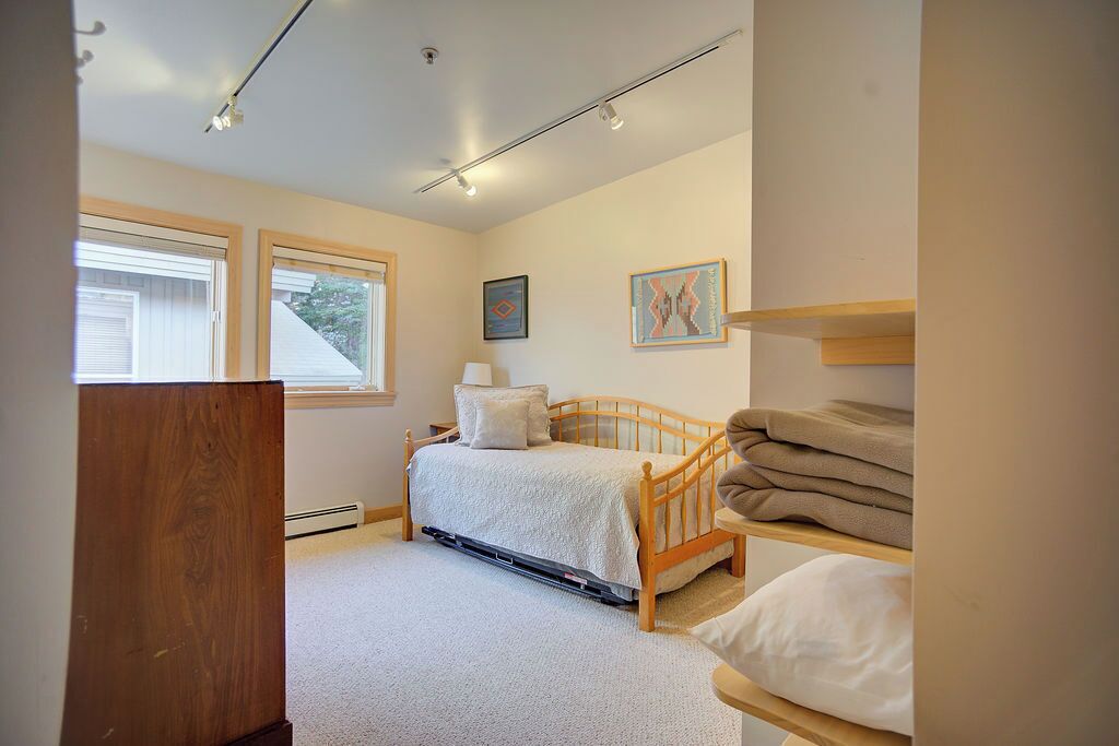 A bedroom with a bed, a window, and a wall-mounted shelf with towels.