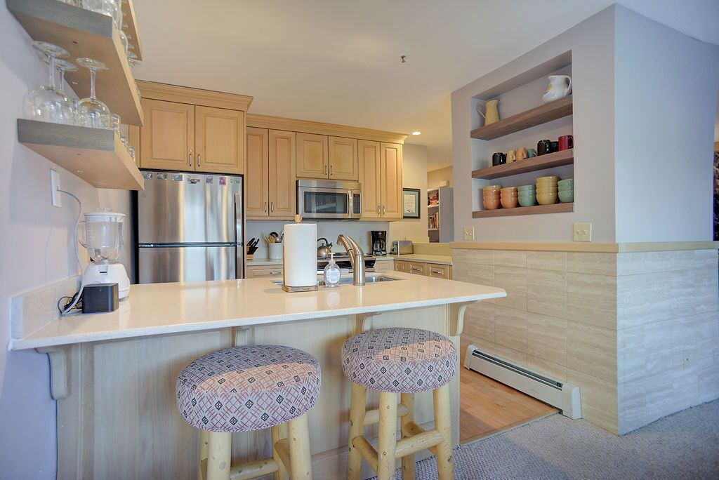 A modern kitchen with wooden cabinets, stainless steel appliances, and a central island with stools.