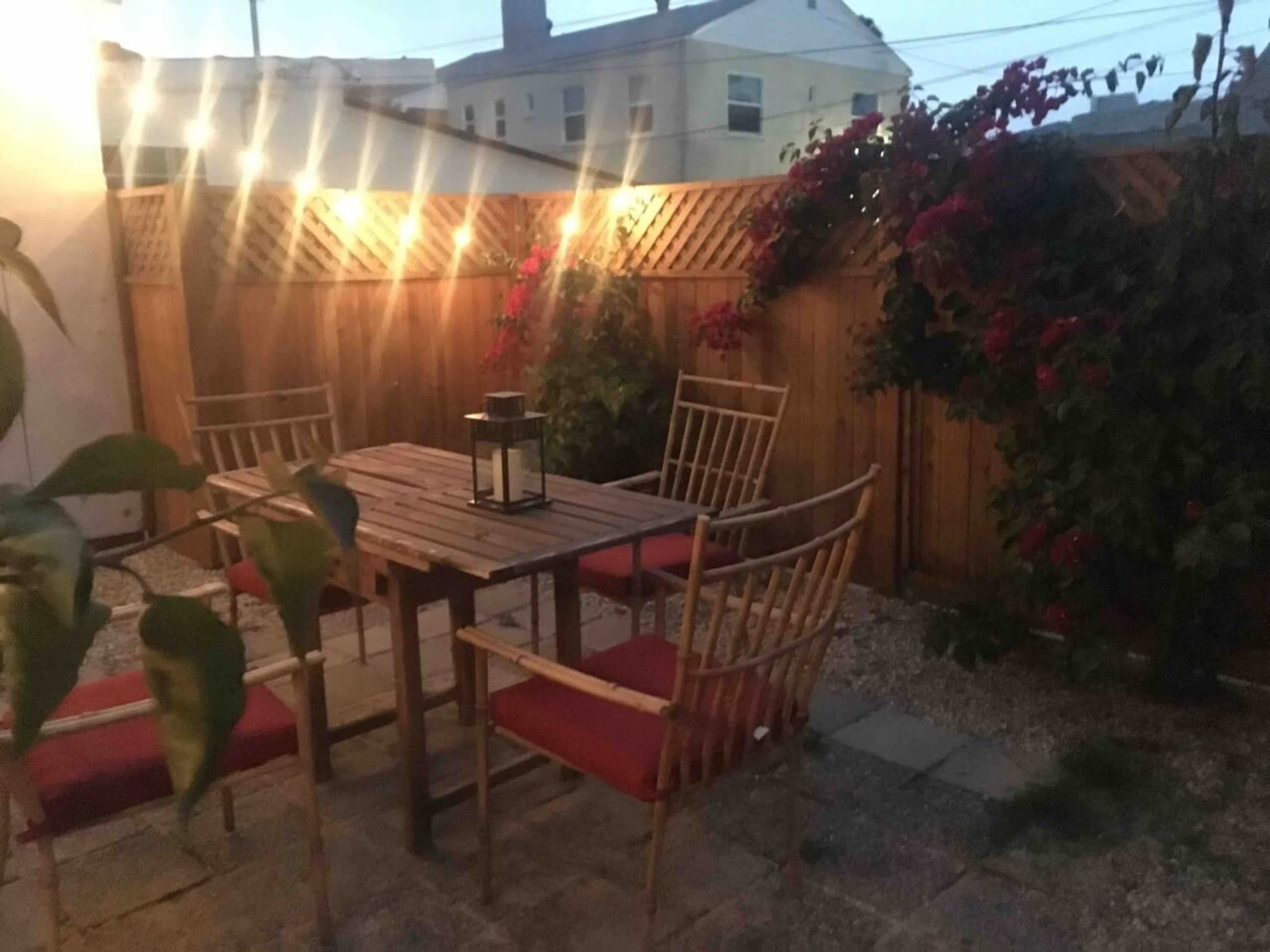 An outdoor patio with a wooden table and chairs, a lantern, and a decorative fence.