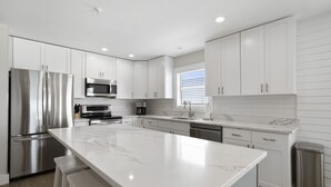 Una cucina moderna con mobili bianchi, un frigorifero in acciaio inossidabile, un forno a microonde e un'ampia isola in marmo.