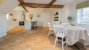 A spacious kitchen with wooden beams, a dining area with a round table, and a view of the outdoors. - The Hop Kiln and The Hayloft are two unique and attractive holiday lets (Monkland nr Leominster)