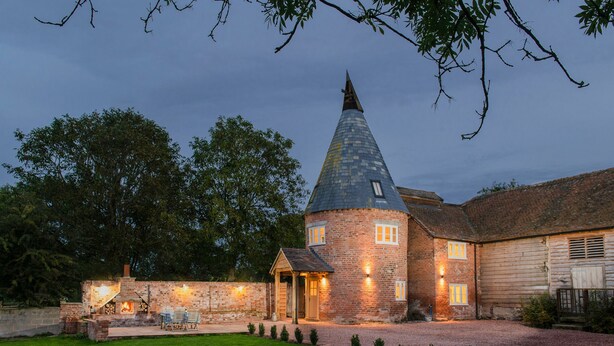 A brick tower with a conical roof, a stone wall, and a small wooden building with a door. - The Hop Kiln and The Hayloft are two unique and attractive holiday lets (Monkland nr Leominster)