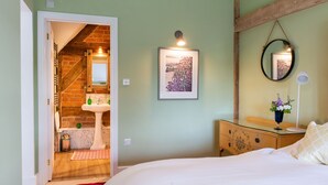 A bedroom with a bed, a dresser, a mirror, a picture on the wall, and a bathroom visible through an open door. - The Hop Kiln and The Hayloft are two unique and attractive holiday lets (Monkland nr Leominster)
