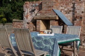 An outdoor seating area with a brick oven, wooden chairs, and a table covered with a patterned tablecloth. - The Hop Kiln and The Hayloft are two unique and attractive holiday lets (Monkland nr Leominster)