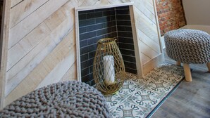 A room with a wooden herringbone wall, a brick wall, a tiled floor, a fireplace, and a small stool. - Elegant & Cozy Escape - 5Beds/2.5Bath - Sleeps 10 (Pittsburgh)
