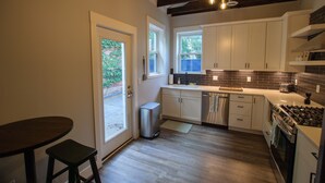 A kitchen with white cabinets, a stainless steel dishwasher, a gas stove, and a window overlooking a garden. - Elegant & Cozy Escape - 5Beds/2.5Bath - Sleeps 10 (Pittsburgh)