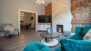 A modern living room with a fireplace, a television, and a dining area visible in the background. - Elegant & Cozy Escape - 5Beds/2.5Bath - Sleeps 10 (Pittsburgh)
