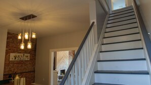 A staircase with white railings and dark steps, leading to a room with a brick wall and hanging pendant lights. - Elegant & Cozy Escape - 5Beds/2.5Bath - Sleeps 10 (Pittsburgh)