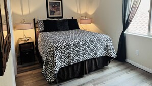Une chambre bien rangée, avec un lit, des lampes de chevet, une petite table et une fenêtre avec des rideaux.