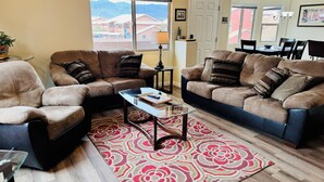 Un salon avec deux canapés, une table basse, un tapis et une vue sur des immeubles par une fenêtre.