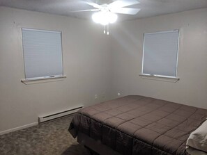 A bedroom with a single bed, two windows with blinds, a ceiling fan, and a wall-mounted heater. - Centrally Located on Pawnee (Pierre)