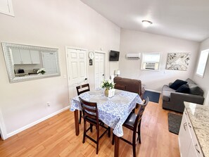 Un comedor con una mesa dispuesta para cuatro personas, un sofá marrón, un sofá gris y un televisor montado en la pared.