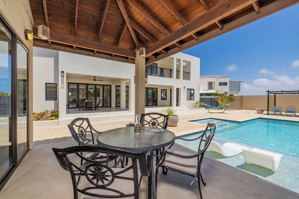 Une terrasse extérieure moderne avec piscine, comprenant un espace salon couvert et une vue sur un immeuble à plusieurs étages.