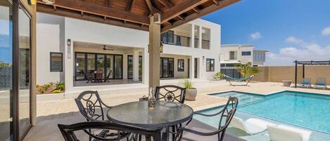 Une terrasse extérieure moderne avec piscine, comprenant un espace salon couvert et une vue sur un immeuble à plusieurs étages.