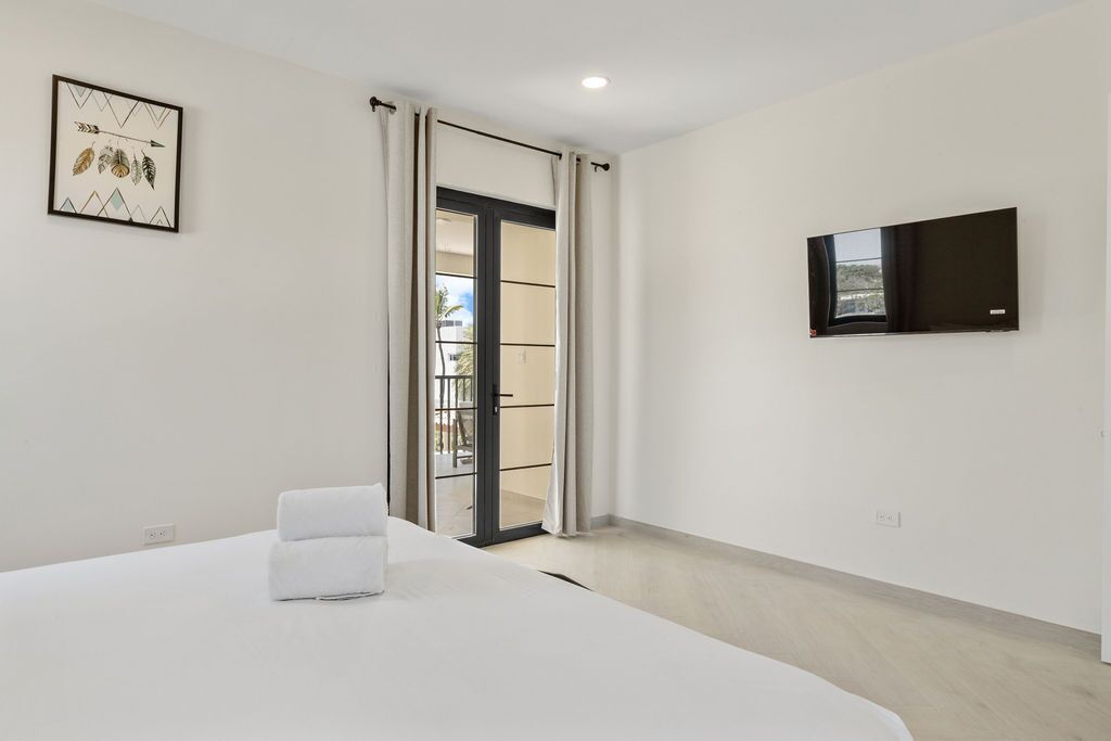 Ein modernes Hotelzimmer mit einem großen Bett, einem flachbildfernseher an der Wand und einer Glasschiebetür, die zu einem Außenbereich führt.