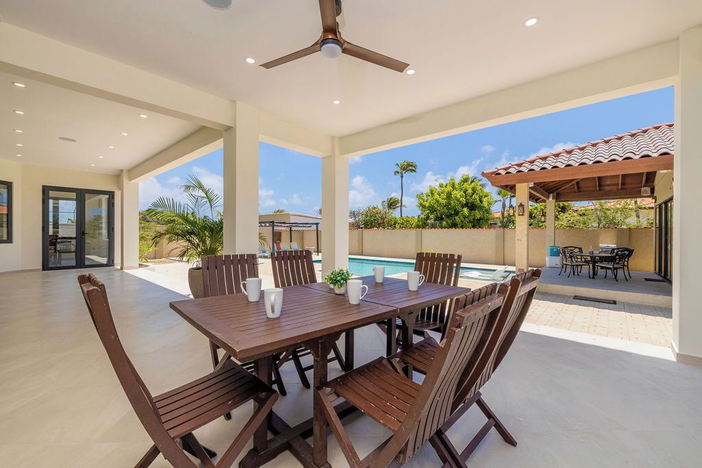 Un patio amplio con piscina, mesa y sillas de madera, y un ventilador de techo.