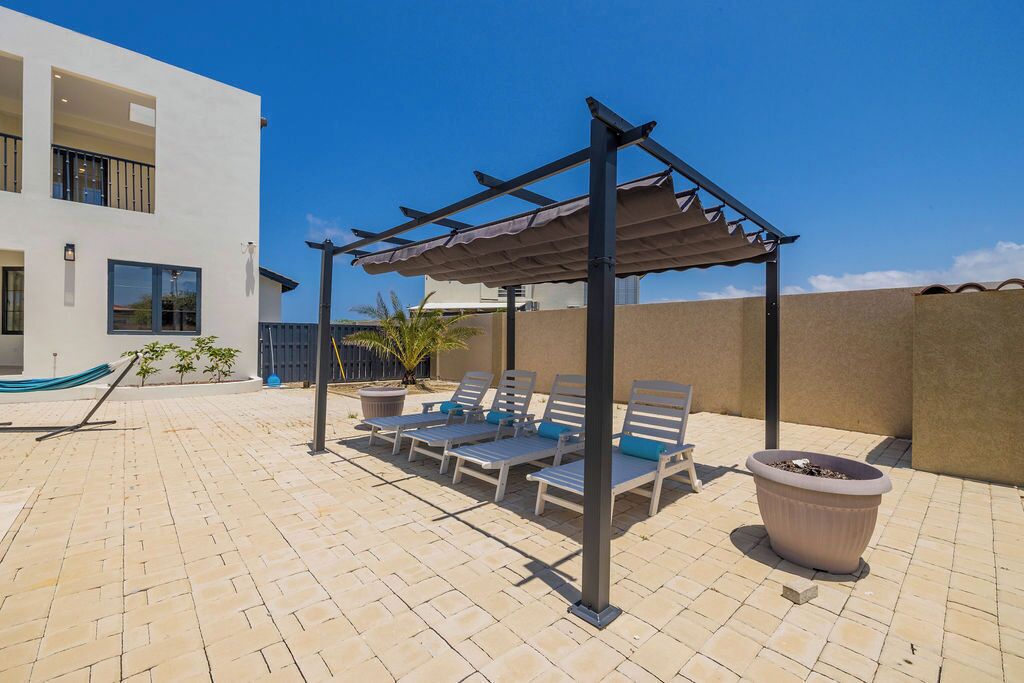 Un patio exterior moderno con pérgola, sillones de descanso y plantas en macetas.