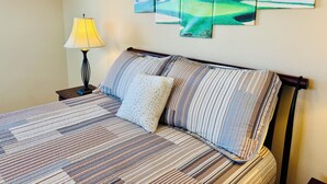 Ein ordentlich bezogenes Bett mit Streifenmuster, eine Lampe auf einem Nachttisch und eine Wand mit drei gerahmten Bildern von einem Golfplatz und dem Meer.