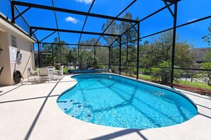 A swimming pool with a glass enclosure, surrounded by white lounge chairs and a white building. - Spacious 4bdm pool house close to Disney (Kissimmee)