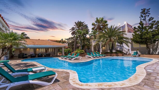 A swimming pool with lounge chairs, palm trees, and a building with a tiled roof.