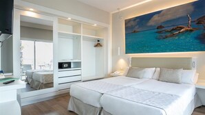 A modern bedroom with a large bed, built-in wardrobe, and a painting of a tropical beach. - Sirenis Club Aura (Sant Josep de sa Talaia)