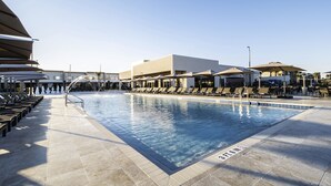 En swimmingpool med solstolar och parasoller, omgiven av byggnader.