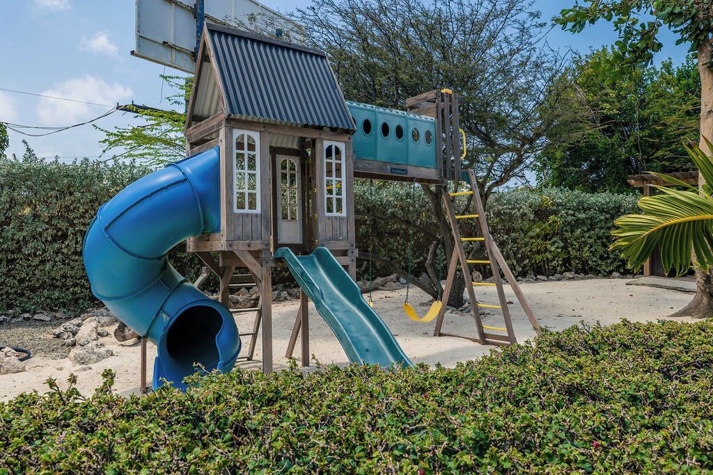 Une structure de jeu en bois, dotée d’un toboggan et d’une zone d’escalade, entourée de verdure.