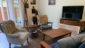 Ein gemütliches Wohnzimmer mit Sofa, Sessel und Couchtisch. Ein Kamin, ein Fernseher und Kunstwerke an der Wand sind zu sehen.