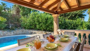 Un área de comedor al aire libre con vista a la piscina, mesas dispuestas y una pérgola.