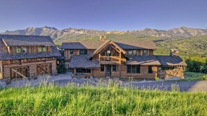 A rustic log cabin with multiple rooms, set against a mountainous backdrop.