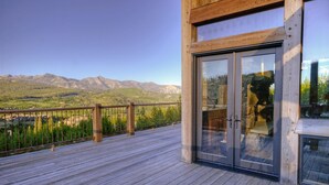A wooden deck with glass doors leading to a room, overlooking a mountainous landscape.