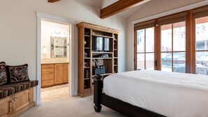 A bedroom with a large bed, wooden built-in shelving, a vanity with a mirror, and a window with a view of the outside. - Little Empire (Park City)