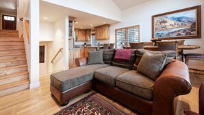 A spacious living area with a large sectional sofa, wooden flooring, and a staircase leading to another level. - Little Empire (Park City)