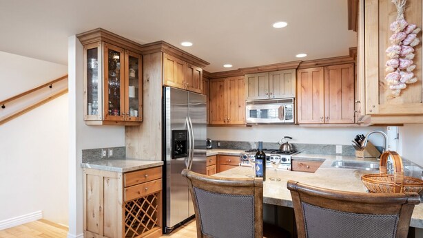 A kitchen with wooden cabinets, a stainless steel refrigerator, a gas stove, and a dining area with two chairs. - Little Empire (Park City)