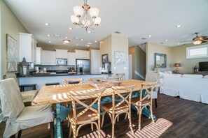 A spacious kitchen with white cabinets, a dining area with a wooden table and chairs, and a living room with a white sofa and a TV. - Scallop Pass (Port St. Joe)
