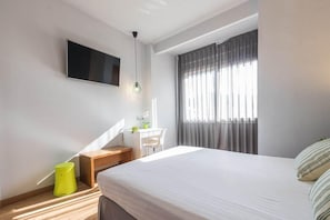 A modern bedroom with a bed, a desk, a chair, a TV, and a window with curtains. - Hotel Margarit (Girona)