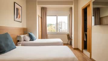 Una habitación de hotel con dos camas, una ventana con cortinas, una silla y un armario.