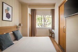 Une chambre d’hôtel avec un lit, un bureau, une télévision et une fenêtre avec des rideaux.