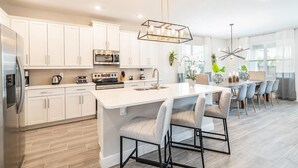 A modern kitchen with white cabinets, a central island, and a dining area with grey chairs.
