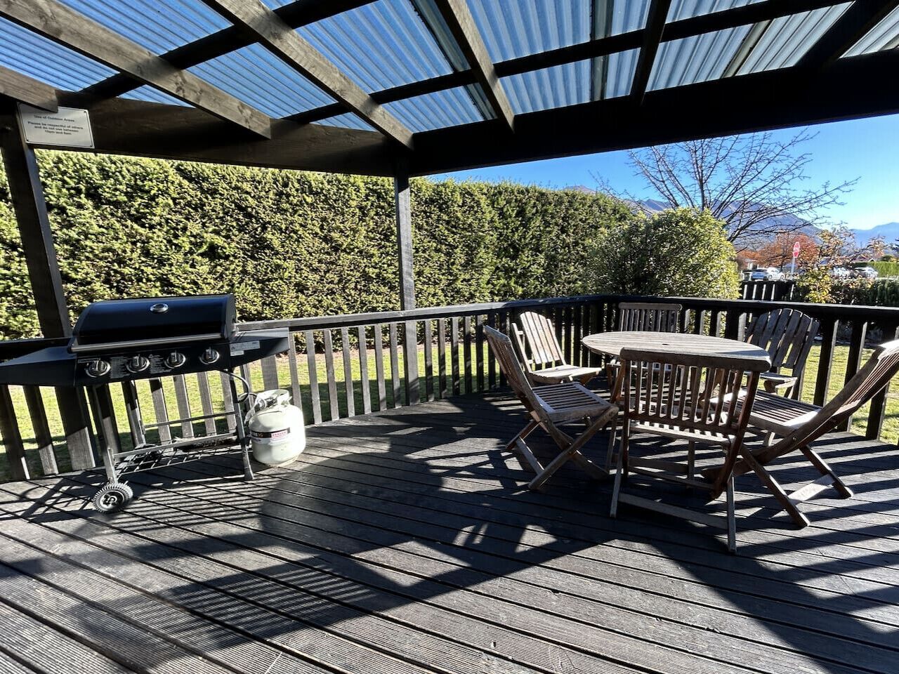 A covered deck with a grill, chairs, and a table.