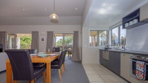 A modern kitchen with a dining area, large windows, and a view of greenery.